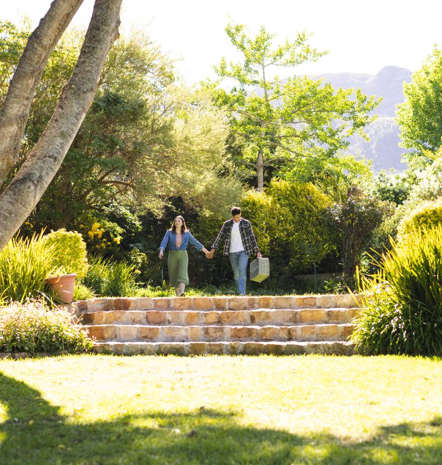 Happy diverse couple walking, holding hands and holding picnic basket in sunny garden, copy space. Outdoors, leisure, love, togetherness and nature unaltered. Garten- und Landschaftsbau auf Usedom
